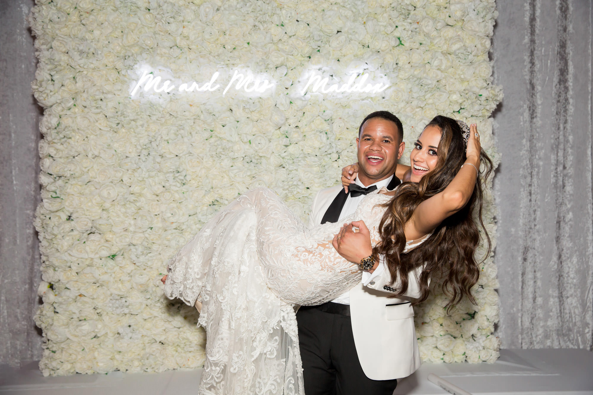 groom holds his bride infront of a Mr & Mrs sign on a floral wall on their wedding day at Ritz-Carlton Key Biscayne