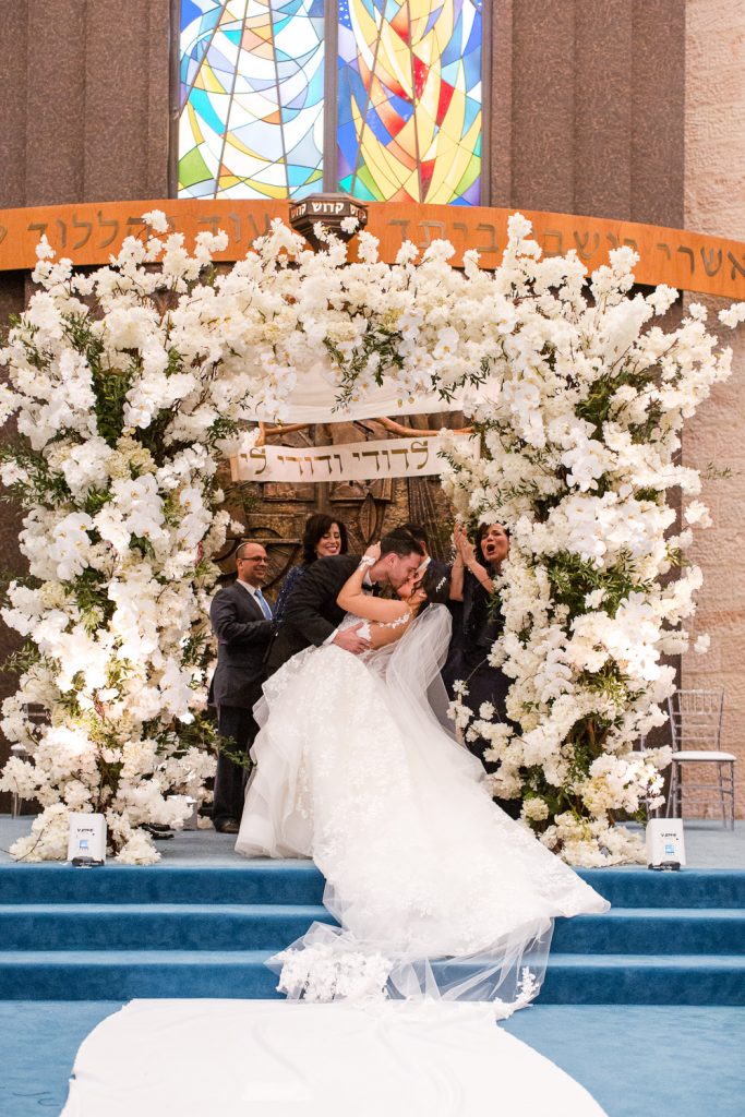 Bride and groom have a first kiss underneath their chuppah during their wedding ceremony at Beth Torah in Aventura.