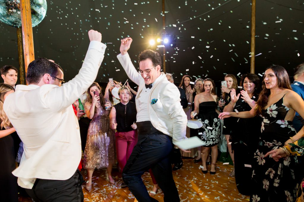 Two grooms dance under a disco ball during their backyard wedding ceremony.