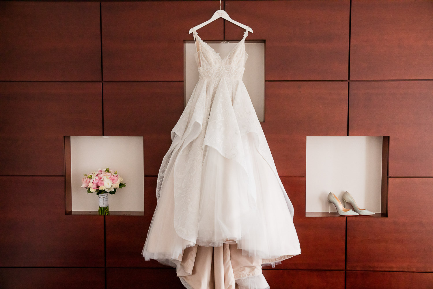 A wedding dress hangs on a personalized hanger in a bridal suite.