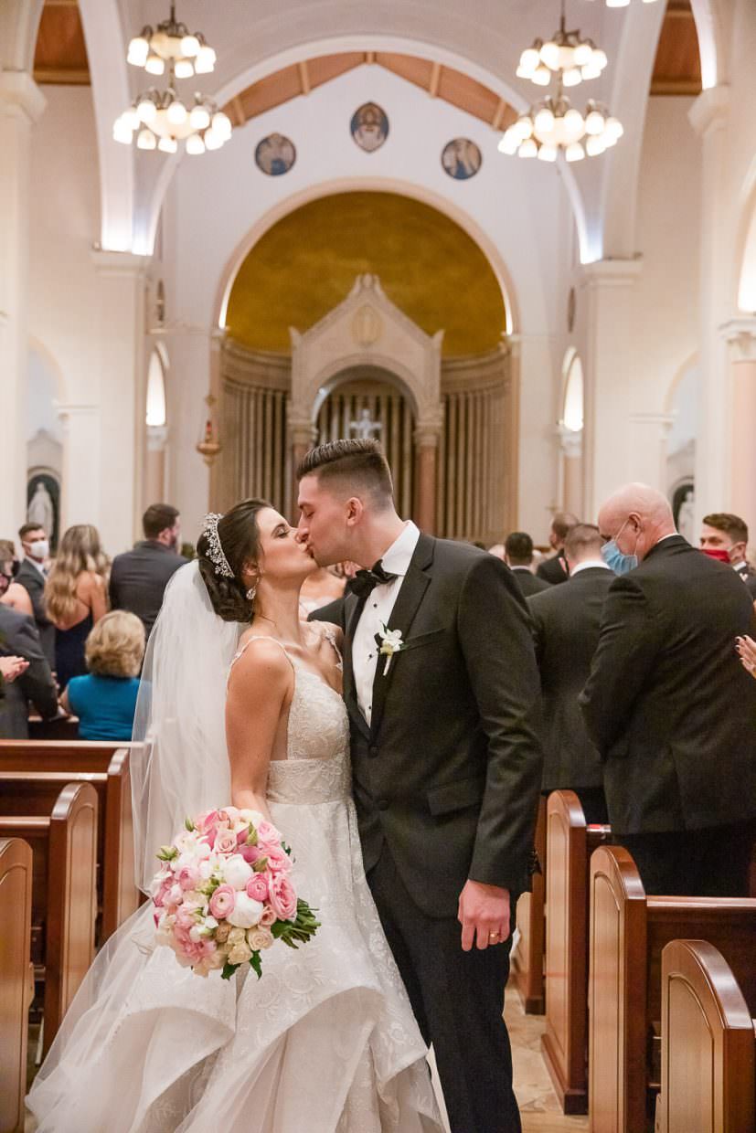 A wedding couple kisses at the end of the aisle in St. Patrick's Church on Miami Beach.