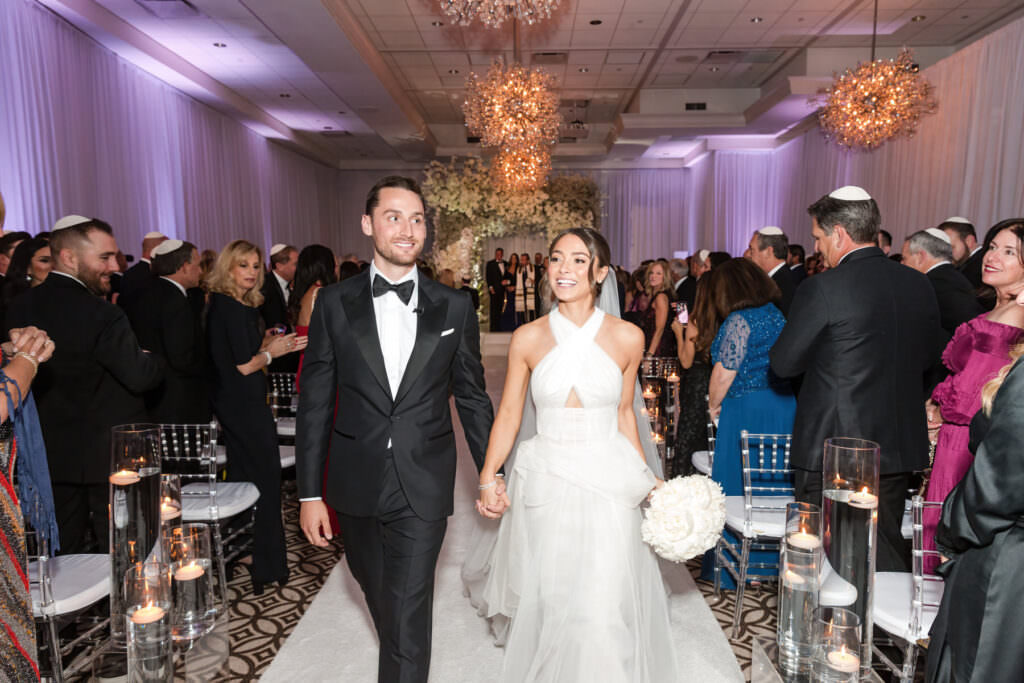 Bride and groom walking down the aisle beneath the chuppah moments after saying I do