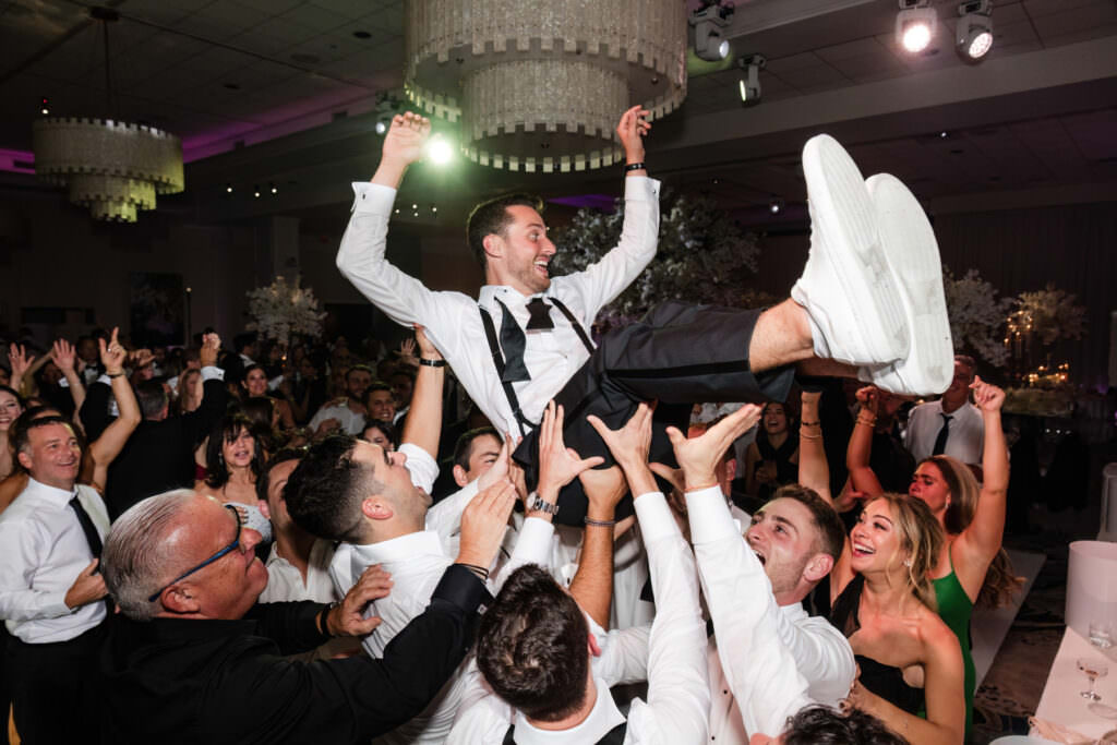 Bride and groom crowd surfing above their guests during an energetic wedding reception