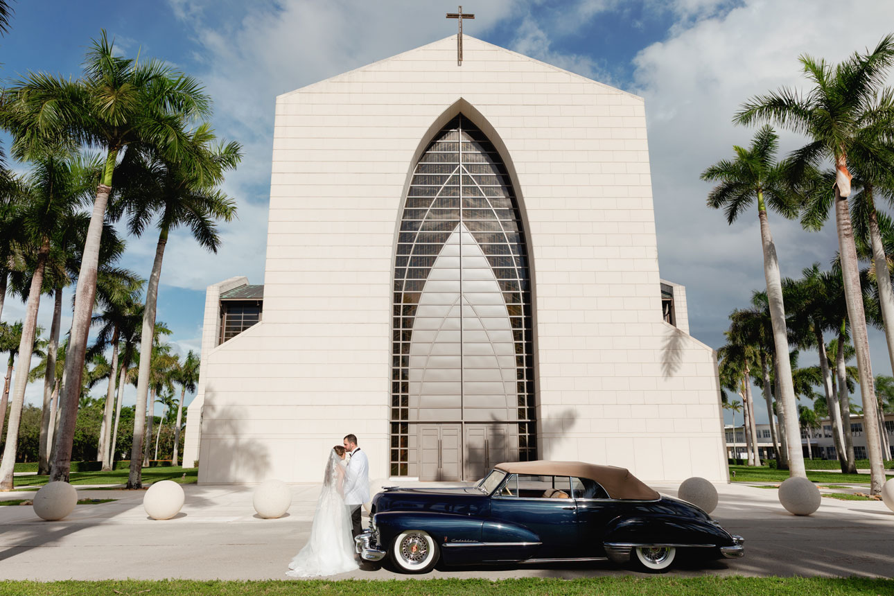 Bride and groom with a classic blue rolls royce pose for a portrait in front of Epiphany Church after their wedding ceremony.