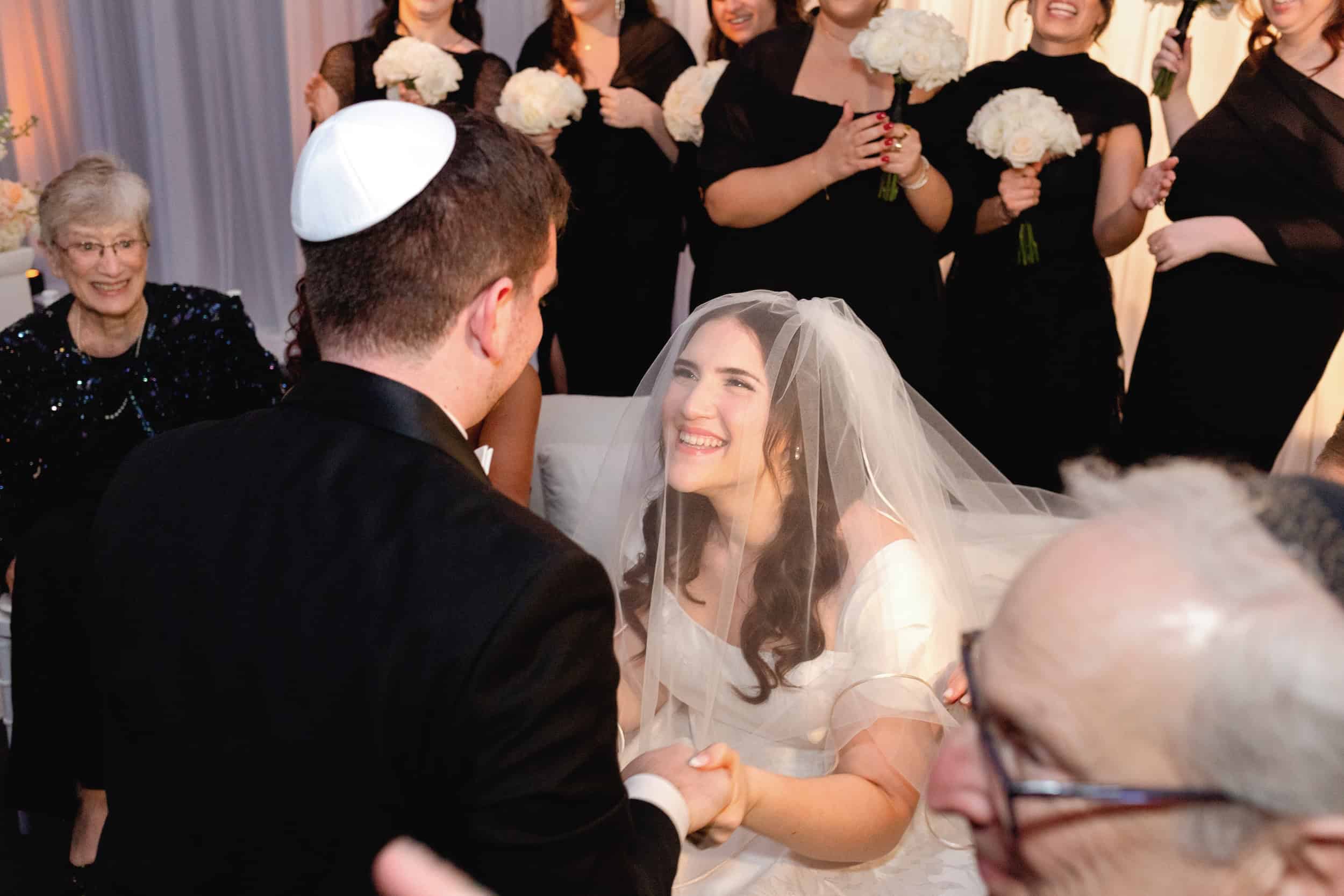 Bride and groom exchanging vows, smiling joyfully during wedding ceremony, surrounded by family and friends.