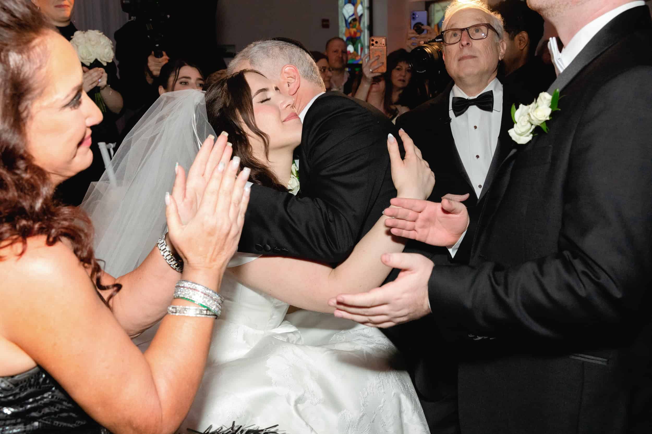 Bride and groom share a heartfelt embrace during their wedding reception, surrounded by family and friends in a joyful moment.