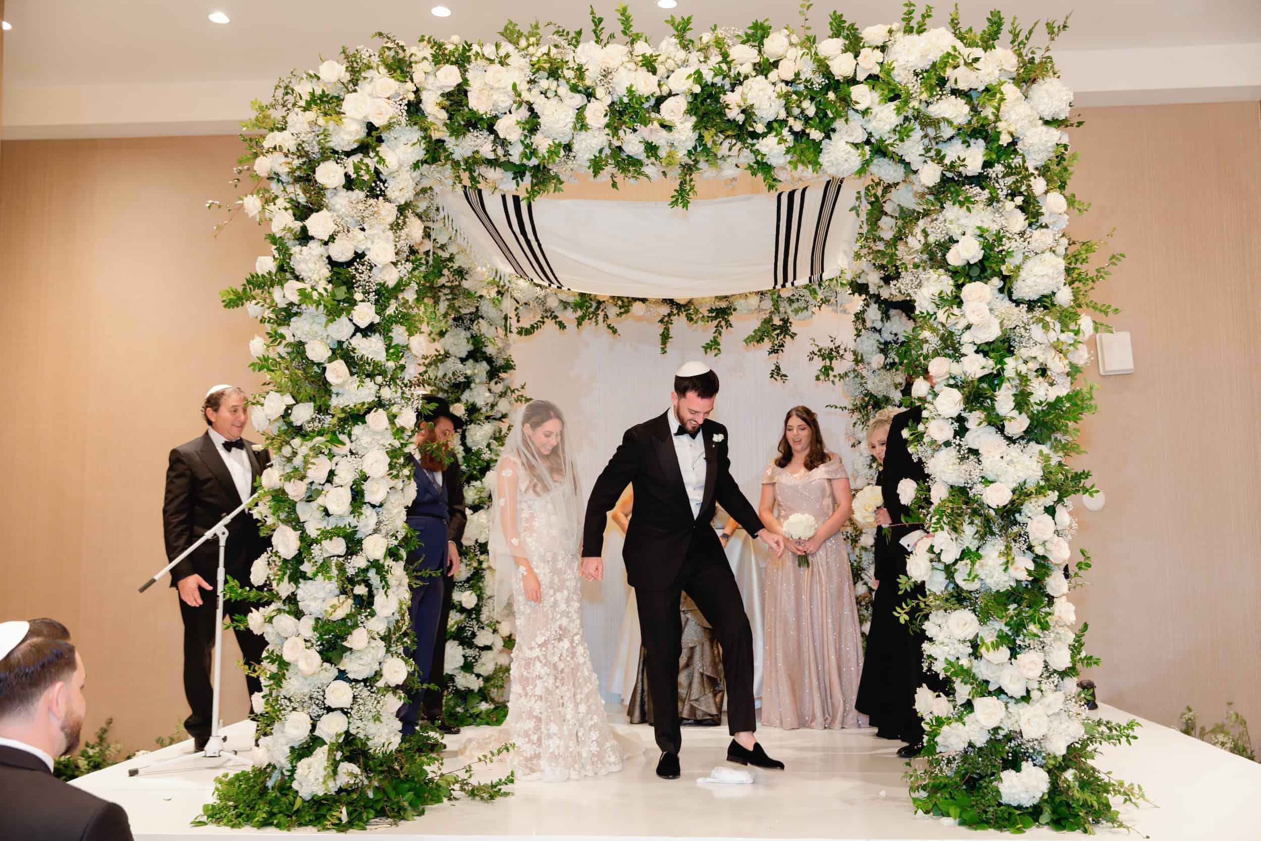 Bride and groom holding hands under a floral arch during their wedding ceremony.
