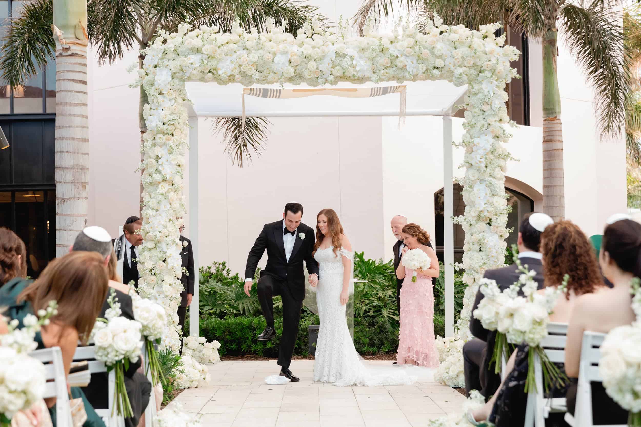 Bride and groom holding hands under a floral arch during their wedding ceremony.