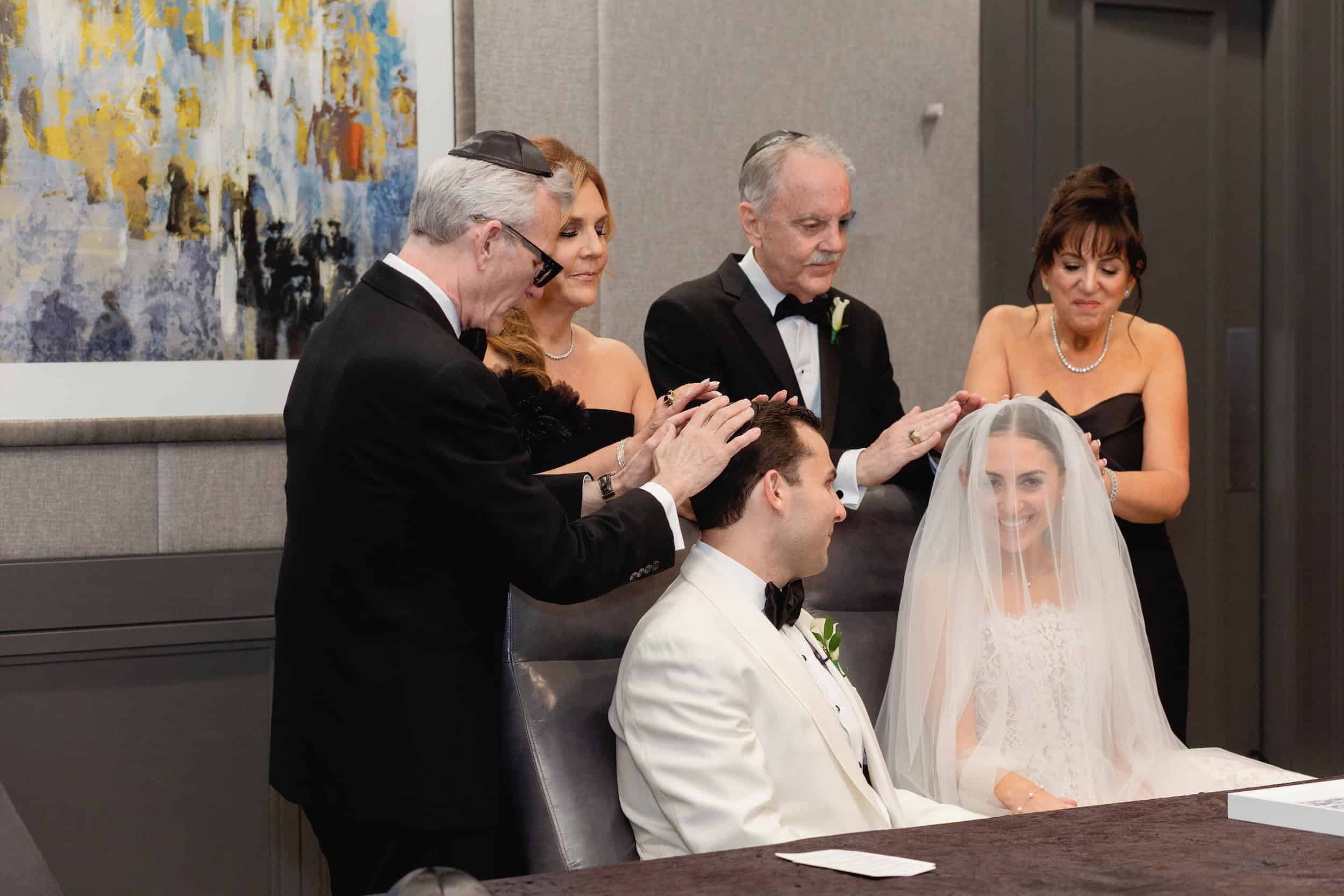 Bride and groom during a Jewish wedding ceremony, groom receiving a traditional blessing, joyful atmosphere, indoor setting.
