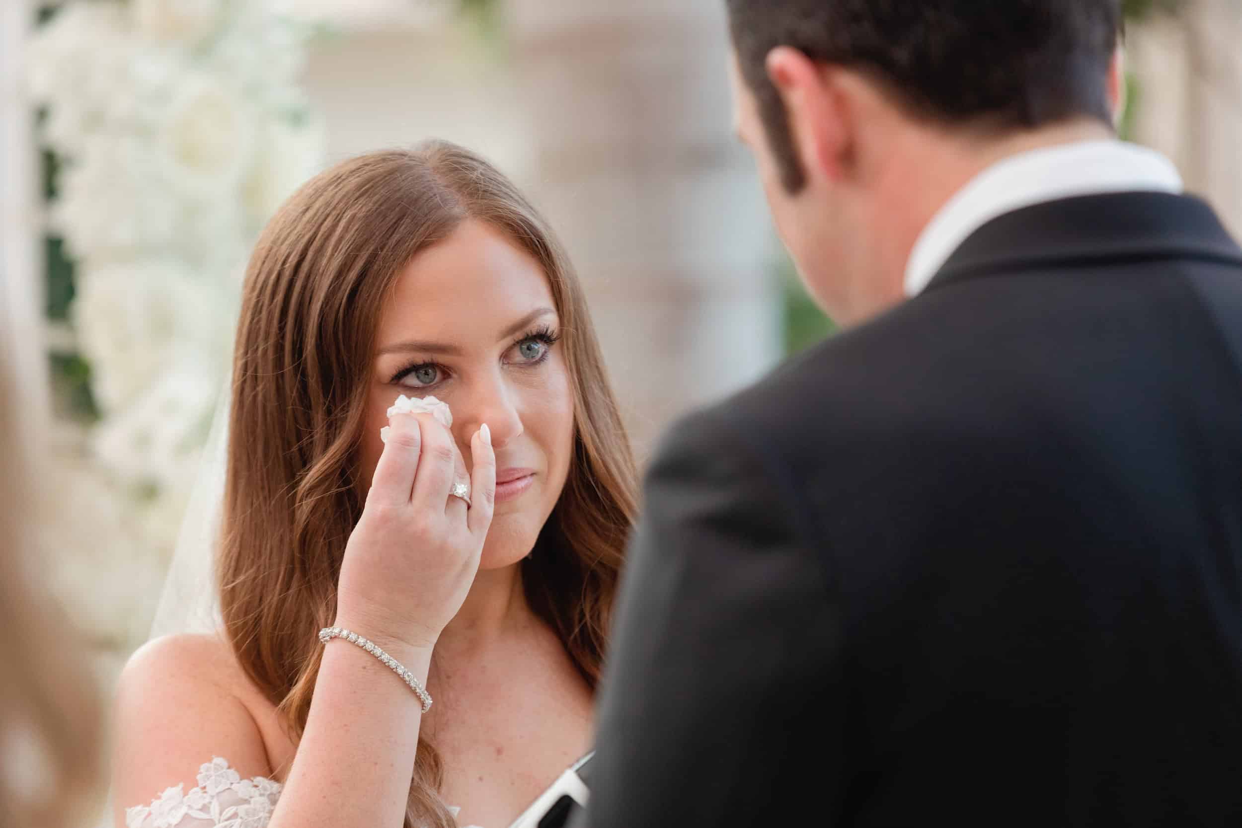 Bride wiping away a tear during her wedding ceremony, emotional moment, soft natural light, elegant setting.