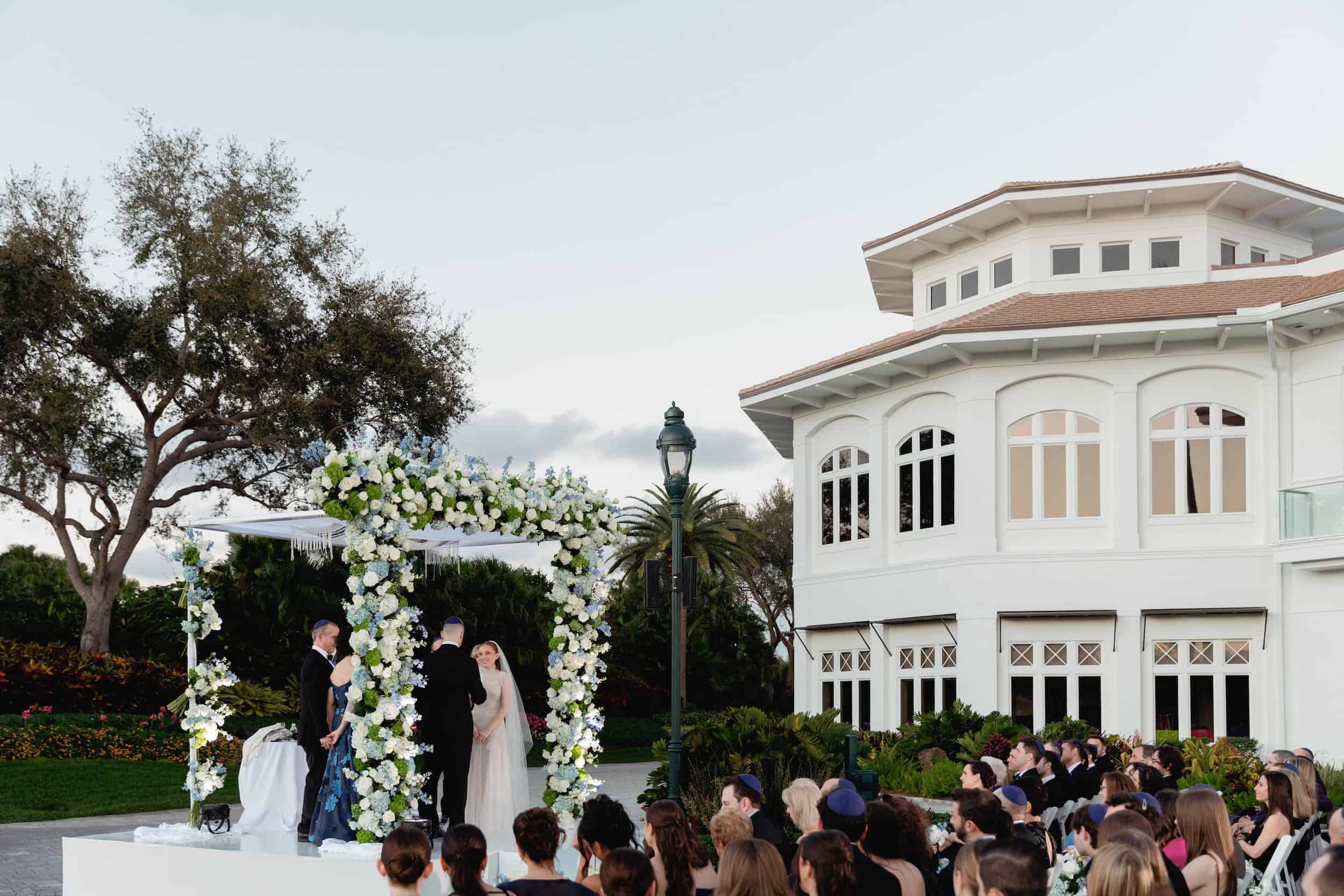Bride and groom exchanging vows under a floral arch during an outdoor wedding ceremony.