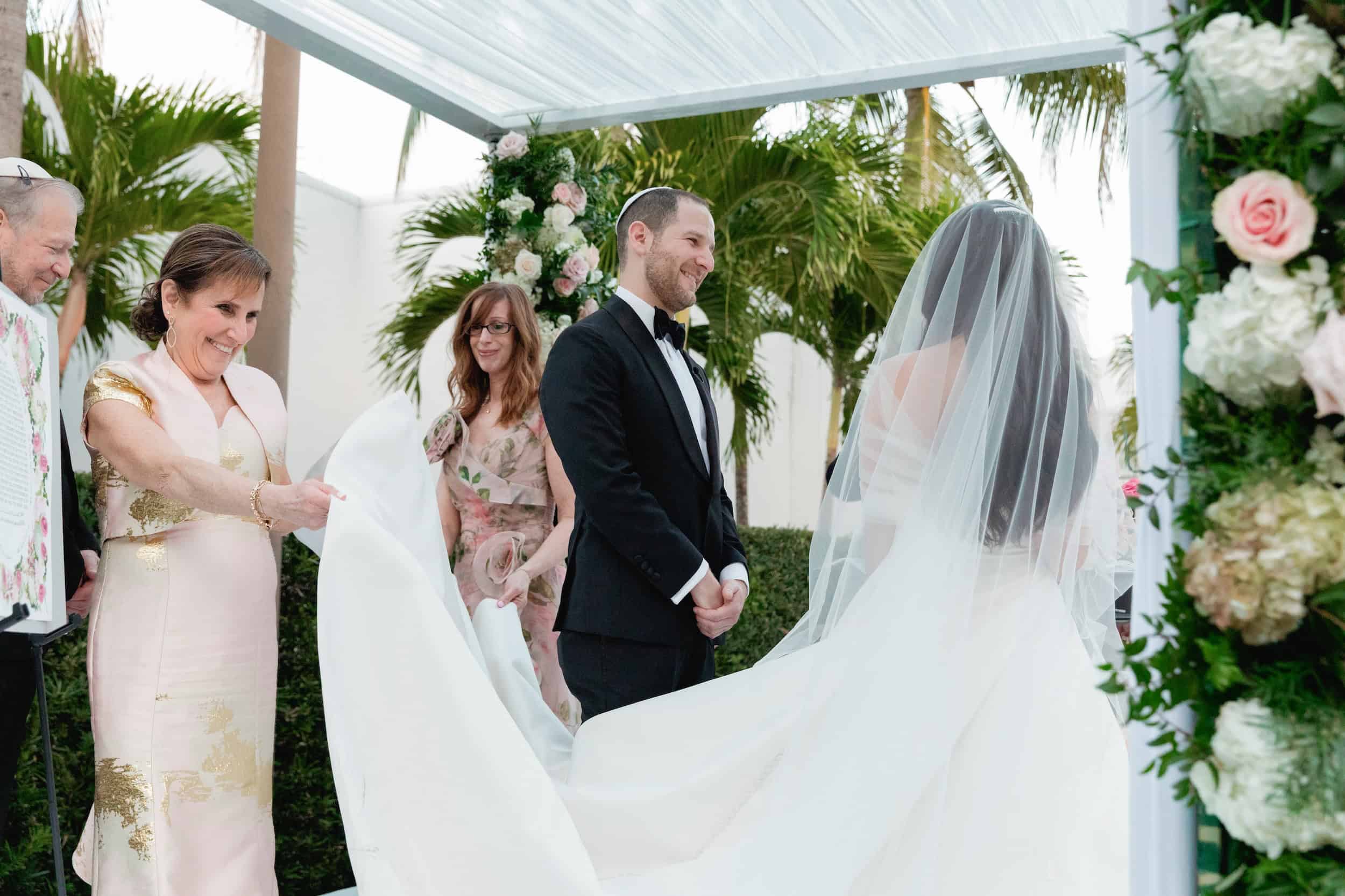 Bride and groom exchanging vows under a floral canopy during a wedding ceremony.