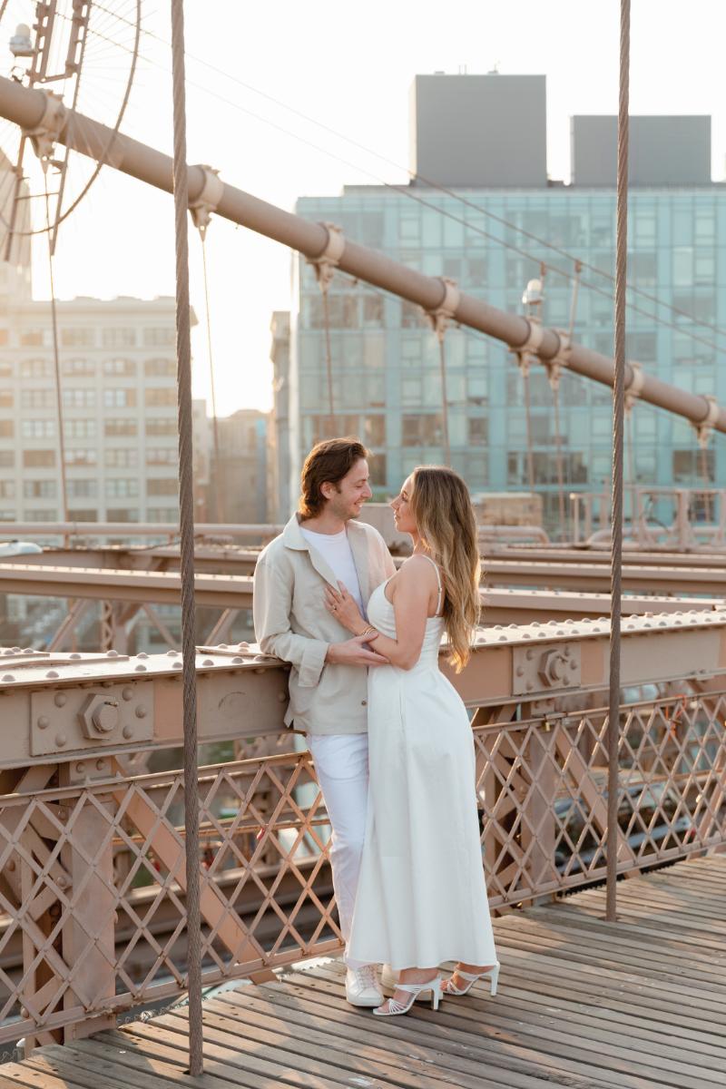 Couple Embraces, Leans Against Railing of Brooklyn Bridge