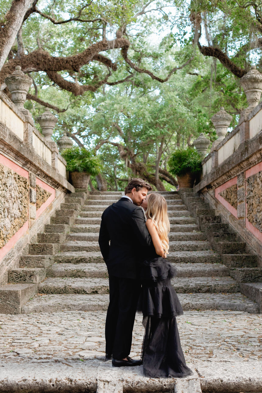 Couple Dressed in Black Tie Formal Attire, Stop for Kiss During Vizcaya Engagement Photos